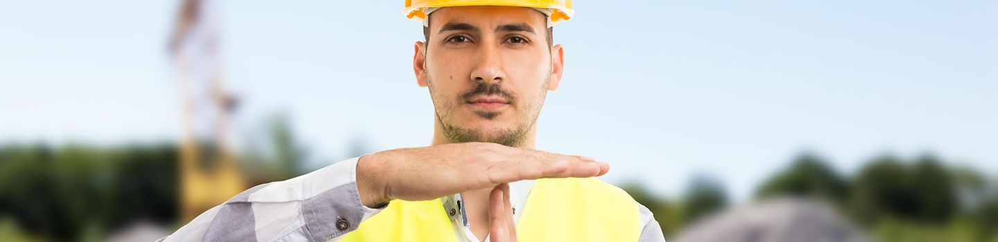 Ein Architekt mit gelber Schutzweste und Helm macht ein Timeout-Zeichen. Ein Architekt mit gelber Schutzweste und Helm macht ein Timeout-Zeichen.