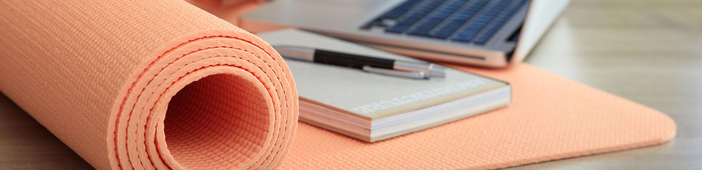 Eine Frau am Schreibtisch, auf dem Yogamatte, Notizblock und Laptop liegen, tippt ins Handy. Eine Frau am Schreibtisch, auf dem Yogamatte, Notizblock und Laptop liegen, tippt ins Handy.