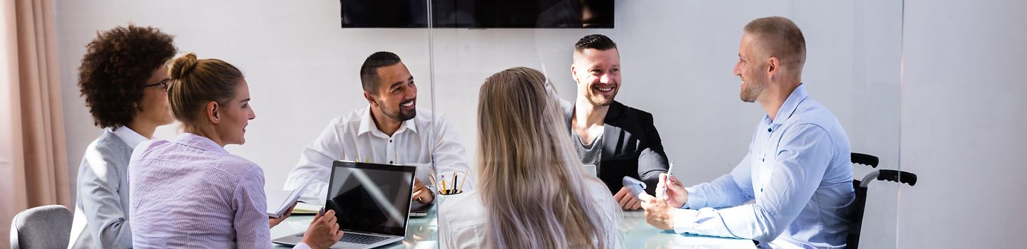 Frauen und Männer sitzen in einer Konferenz um einen Tisch herum