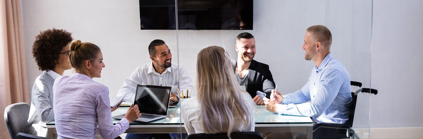 Frauen und Männer sitzen in einer Konferenz um einen Tisch herum